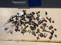 Overhead photo showing the collection of assorted vintage drawer pulls, knobs, and handles scattered on a surface with measuring tape below.