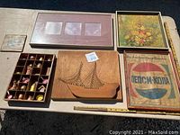 Lot of vintage decorative items on table including framed prints, wooden carving, miniature copper items in a box, and collectible doll