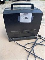 Back view of black GAF 8mm movie projector showing carrying handle, metal panel, and attached power cord on beige surface.