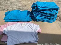 Stack of blue, white, and pink youth T-shirts folded on a surface outdoors
