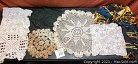 Overview of seven items including various crochet doilies and fabric scarves laid out on a black surface showing condition and variety.