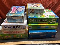 Photo showing stacked board games and puzzles, titles visible include Boggle, Sequence, Monopoly Junior, Robots!, LeapFrog Dominoes, and Fish Pond puzzle.