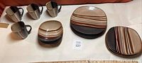 Four dinner plates, four salad/dessert plates, four bowls and four mugs in brown striped stoneware on a white surface
