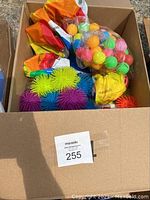 Box of assorted balls showing a variety of colorful spiky balls and a bag of plastic balls inside a cardboard box.