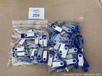 Two large resealable bags containing over 60 blue and silver swivel USB flash drives with Duke branding