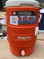 Front view of orange Igloo cooler showing brand label, capacity, and dispensing spigot.