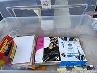 Photo of the large clear plastic tub filled with various mostly new office supplies including calculators, paper reams, file folders, pens, and sticky notes