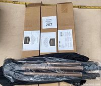 Three boxed Amazon Basics tripods stacked with one tripod outside box wrapped in plastic and carrying bag visible.