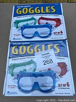 Two unopened boxes with printed text 'Color Safety Goggles', each showing images of colorful goggles in blue, red, and green and stating 'Set of 6' goggles.