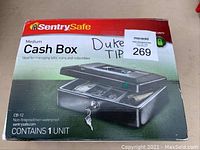 Front view of the sealed SentrySafe medium cash box in original packaging showing branding, model CB-12, and details about use and features.