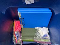 Tub with blue clip binders, index cards, and plastic bags of office supplies