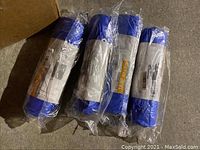 Four blue tarps, new in original plastic packaging, laid on floor.