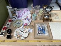 Full view of assorted decorative items including glasses, plates, framed prints, tea pot, and textiles.
