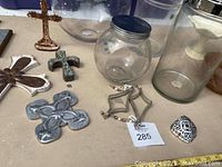 View of large glass jars and mixed decorative metal crosses on table surface