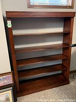 Front view of the large wooden bookcase with four shelves against a wall.