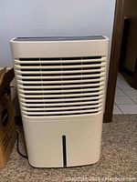 Front view of beige Whirlpool dehumidifier with horizontal air vents and blue water level indicator on tank.