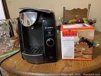 View of Bosch Tassimo coffee maker beside boxed French Cafe Crème Brûlée dessert set on a wooden table.