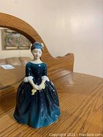 Royal Doulton Cherie porcelain figurine facing front on wooden surface with mirror reflection.