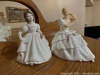 Photo showing front view of two Royal Doulton figurines on a wooden surface.