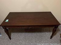 Full front view of desk showing the dark wood finish, legs, and drawer front with decorative carving and a polished surface.