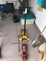 Wide view showing heavy duty yellow garage floor jack, smaller red floor jack, wheel wrench, and small sledgehammer together on garage floor.