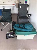 Full view of reclining lounge chair, 2 Coleman Voyager chairs with carrying bags, lunch bag, duffel bag on top of Rubbermaid tote