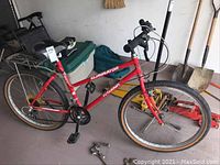 Side view of the full bicycle showing red frame, padded seat, rear carrier, handlebars with bell, and tires.