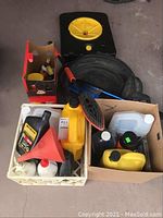 Wide view showing assorted automotive fluid containers, a wash brush, funnel, and ice scraper in crates and box