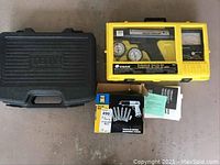 Photo showing a yellow plastic professional timing light set, a black plastic socket set case, and instruction manuals, all arranged on the floor.