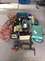 All items in the lot including cords, battery charger, tools, and containers laid out on floor