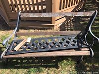 Front view of the garden bench showing the cast iron frame, wooden slats on the backrest and seat, and the detached wooden plank.