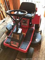 Front angled view of the red Huskee riding lawnmower showing the black steering wheel, seat, and front panel with 10 horsepower branding.
