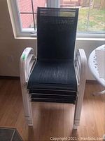 Four stacked white metal frame garden chairs with black mesh seats, photographed from front.