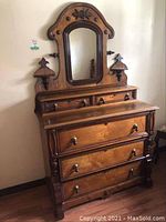 Full front view of wooden dresser with attached central mirror, carved crest and finials
