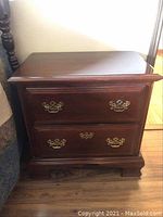 First bedside table with two drawers and brass handles, showing overall condition and wear on wood surfaces
