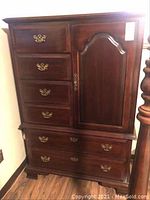 Full front view of tall dresser showing six drawers and one cabinet door with brass handles, dark wood finish.