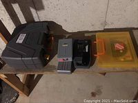 Photo of several hard plastic carrying cases containing the power tools and accessory sets on a wooden workbench.