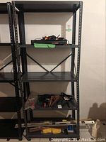 Photo of black metal shelving unit with four shelves holding hand tools and workshop accessories, showing structural frame and cross braces