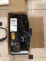 Top view of the angle grinder in the original box, showing the grinder with a grinding disc attached and power cord wrapped inside the box.