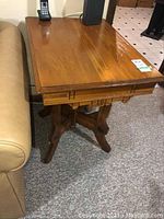 Wood occasional table next to sofa, showing top surface and carved details of legs and aprons.
