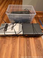 Two Sony electronic devices: a DVD/VHS combo player and a cassette player with cords in a plastic bin and on floor.