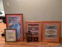 Wide shot showing all five pieces: framed Georgia O'Keefe print, cross stitch sampler, two Aztec woven art pieces, and metal wall hanging.