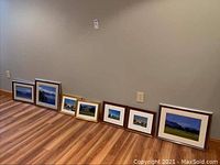 Seven framed photography prints of nature scenes including water, florals, and countryside lined up on floor