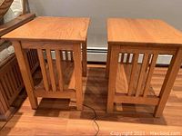 Pair of wooden end tables showing front and side views. Both tables have vertical slatted sides and lower shelves. Wood grain is visible and consistent.