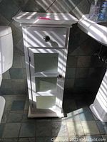 White wooden vanity cabinet beside toilet and sink, showing one drawer and frosted glass door.