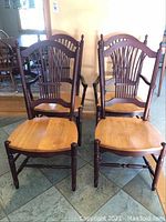 Four wooden dining chairs with oak color seats and brown stained backs and legs; two have armrests (captains).