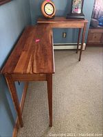 Two wood console tables placed side by side against a wall with a clock and a decorative item on top.