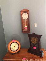 Three wooden clocks displayed, including wall-hanging Kieninger pendulum clock and two table clocks on wood surface.