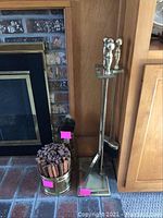 Full view of metal fireplace tool set and metal bucket with wood fire starters by fireplace.