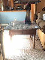 Wooden side table with polished granite top, showing drawer front and tapered wooden legs from front view.